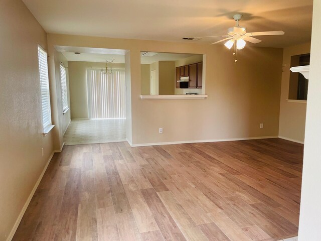 unfurnished living room with light wood-style floors, baseboards, ceiling fan with notable chandelier, and visible vents