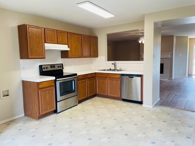 kitchen with brown cabinetry, appliances with stainless steel finishes, a sink, light countertops, and under cabinet range hood