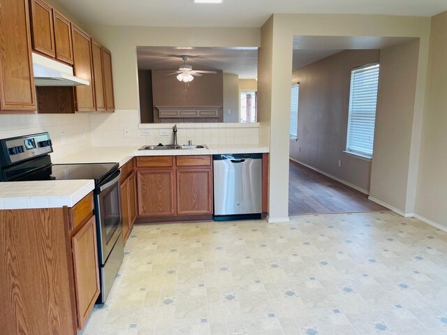 kitchen featuring a ceiling fan, backsplash, a sink, under cabinet range hood, and stainless steel appliances