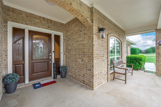 view of exterior entry featuring a porch and brick siding