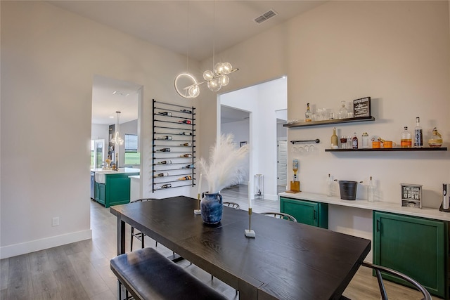 dining room with a bar, a notable chandelier, wood finished floors, and visible vents