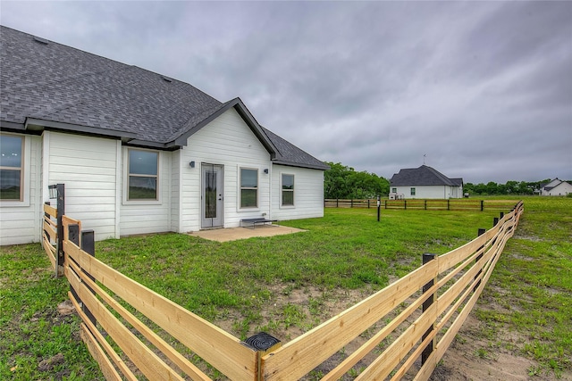 back of property featuring fence, a shingled roof, a lawn, and a patio area