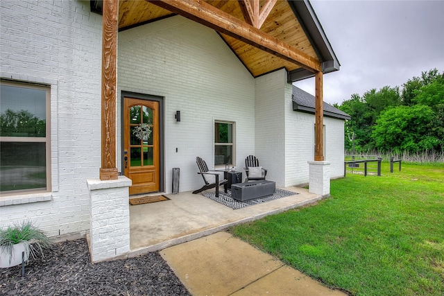 view of exterior entry with a lawn, brick siding, and a patio area