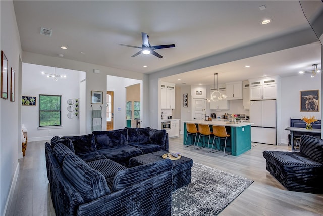 living area featuring light wood-style floors, ceiling fan with notable chandelier, recessed lighting, and visible vents
