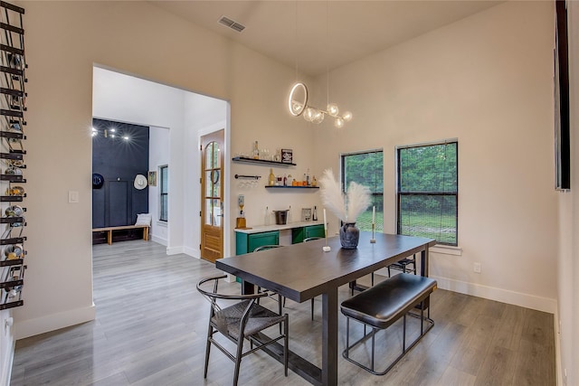 dining space with baseboards, visible vents, wood finished floors, and a towering ceiling