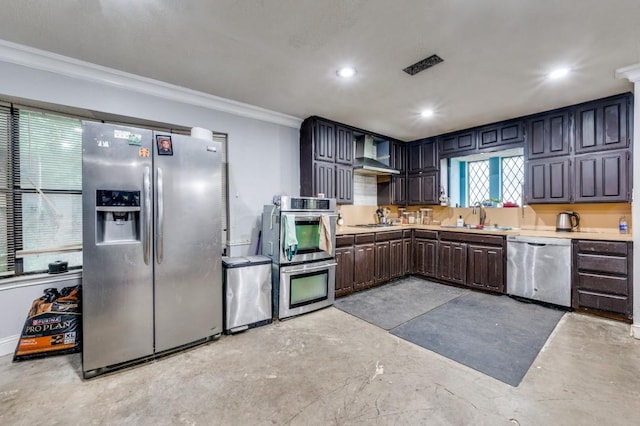 kitchen with wall chimney range hood, appliances with stainless steel finishes, a sink, concrete floors, and ornamental molding
