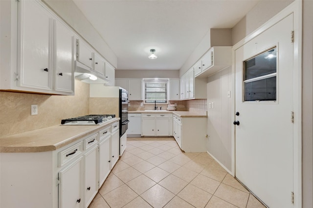 kitchen featuring gas cooktop, light countertops, under cabinet range hood, tasteful backsplash, and a sink
