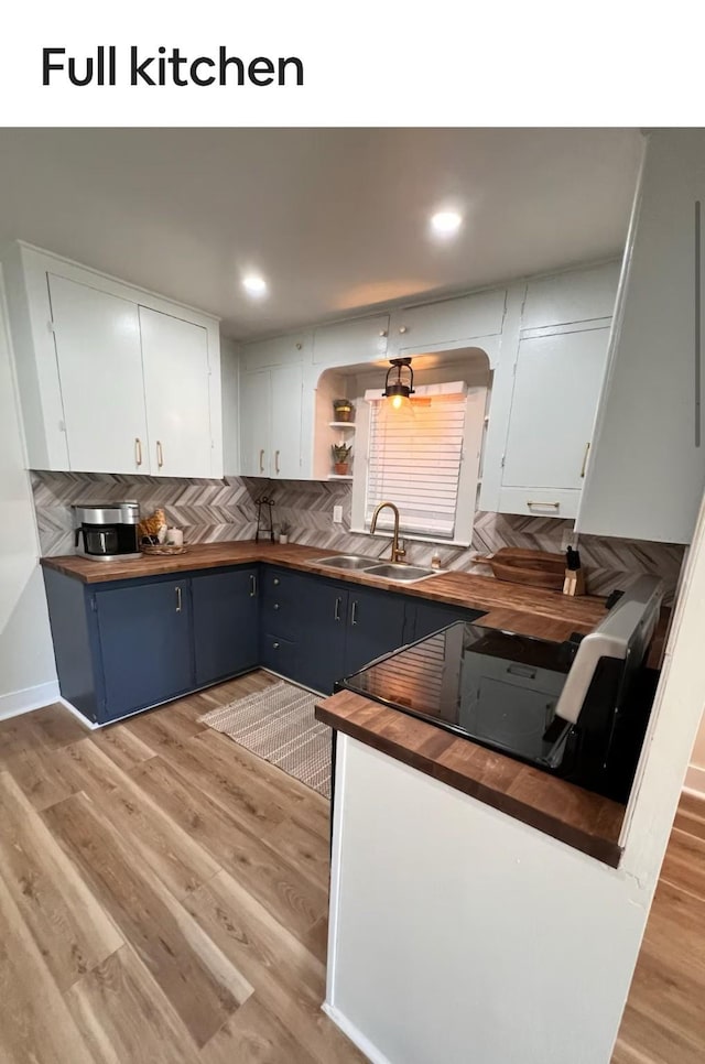 kitchen featuring butcher block countertops, arched walkways, blue cabinets, a sink, and light wood-style flooring
