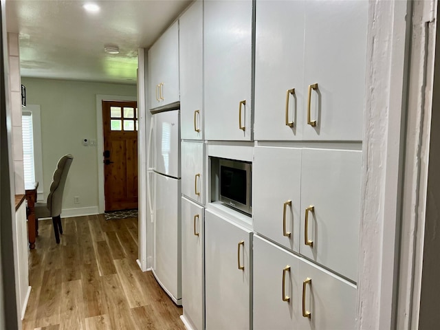 kitchen with baseboards, freestanding refrigerator, stainless steel microwave, light wood finished floors, and white cabinetry