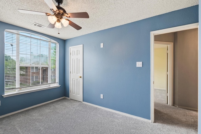 carpeted spare room with baseboards, ceiling fan, a textured ceiling, and visible vents