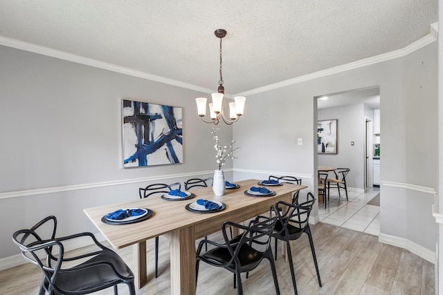 dining space with a notable chandelier, a textured ceiling, light wood-style flooring, baseboards, and ornamental molding