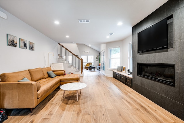 living area with visible vents, a tiled fireplace, light wood-type flooring, stairs, and recessed lighting