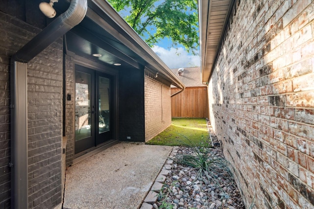 view of side of home with brick siding, fence, and french doors