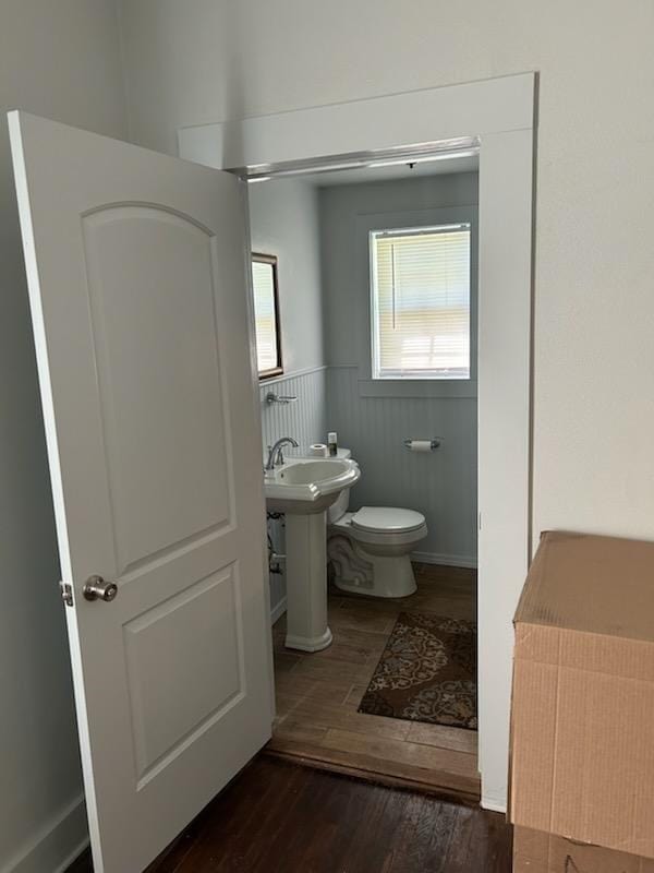 half bathroom with wainscoting, toilet, and wood finished floors