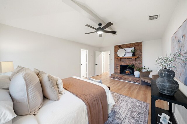 bedroom with a ceiling fan, a brick fireplace, light wood finished floors, and visible vents