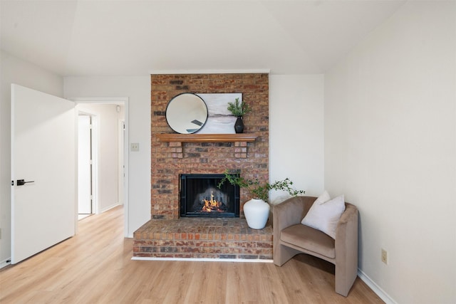 living room with vaulted ceiling, baseboards, a brick fireplace, and wood finished floors