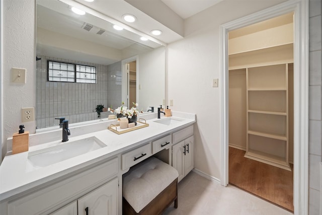 full bath with double vanity, recessed lighting, a walk in closet, and a sink