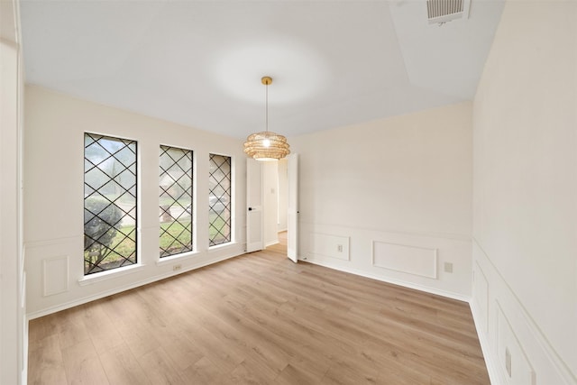 unfurnished room featuring wainscoting, a decorative wall, light wood-type flooring, and visible vents