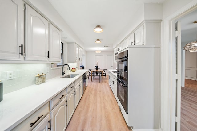 kitchen with light wood-style floors, a sink, decorative backsplash, and white cabinetry