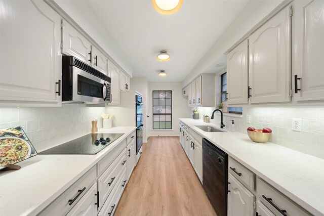 kitchen featuring white cabinets, a sink, black appliances, and light wood-style floors