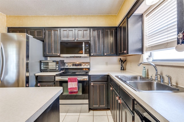 kitchen with appliances with stainless steel finishes, a sink, light tile patterned floors, a toaster, and light countertops