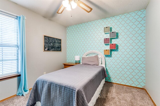carpeted bedroom with an accent wall, baseboards, wallpapered walls, a textured ceiling, and a ceiling fan