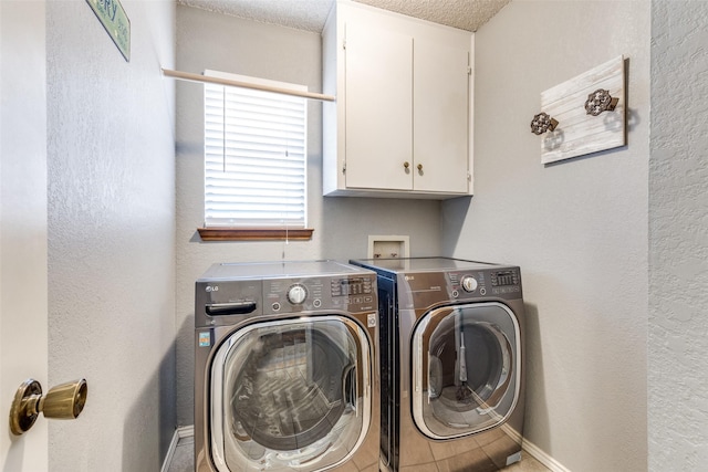 clothes washing area featuring baseboards, a textured wall, washing machine and dryer, and cabinet space