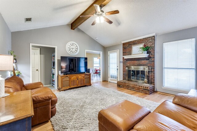 living room featuring a fireplace, light wood-style flooring, a ceiling fan, vaulted ceiling with beams, and visible vents