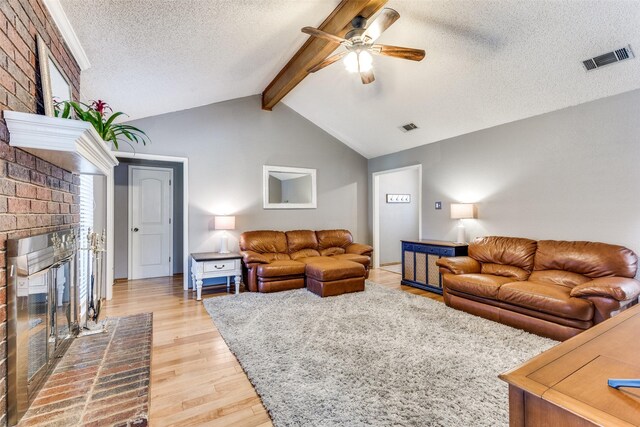 living room with visible vents, a brick fireplace, ceiling fan, a textured ceiling, and light wood finished floors