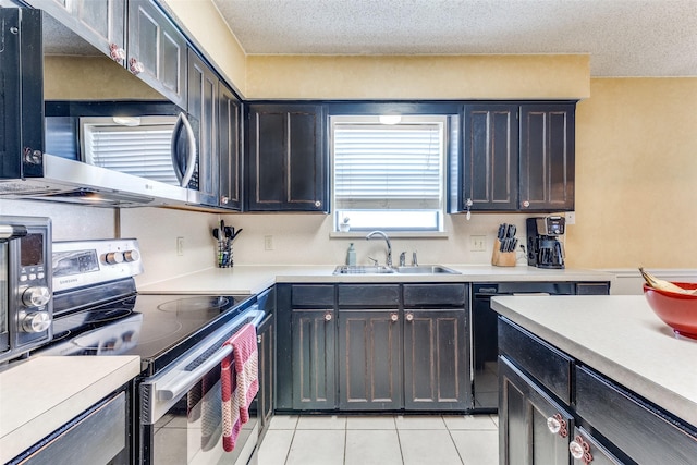 kitchen featuring a textured ceiling, appliances with stainless steel finishes, a sink, light tile patterned floors, and light countertops