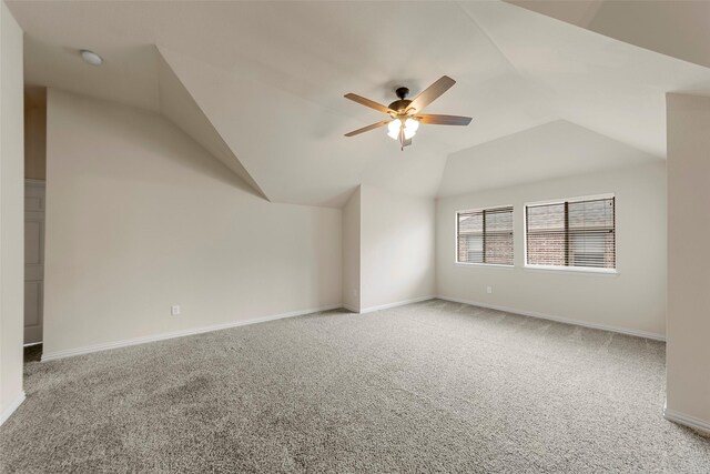 empty room with carpet flooring, a ceiling fan, baseboards, and vaulted ceiling