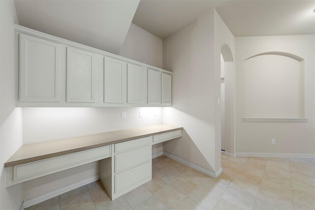 unfurnished office with built in study area, baseboards, and arched walkways
