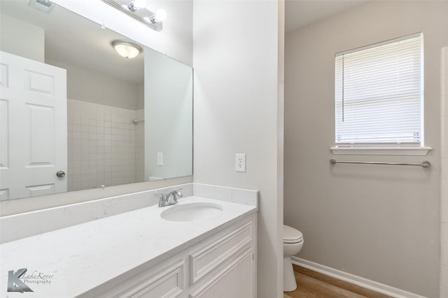 bathroom with vanity, toilet, wood finished floors, visible vents, and tiled shower