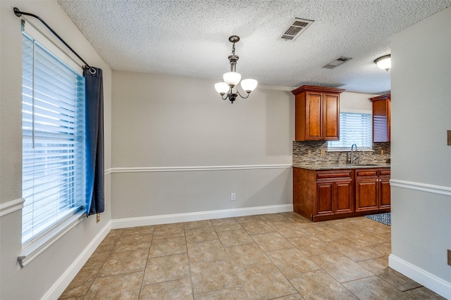 2909 Chisholm Trl, Corinth, TX 76210 - kitchen with a sink, decorative backsplash, hanging light fixtures, brown cabinetry, and a chandelier