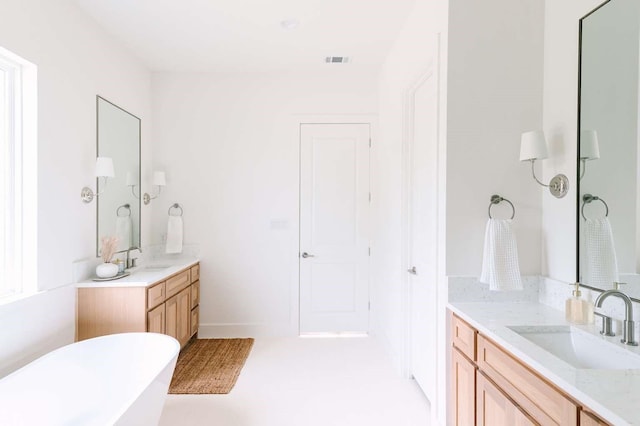 full bath with a sink, visible vents, a soaking tub, and two vanities