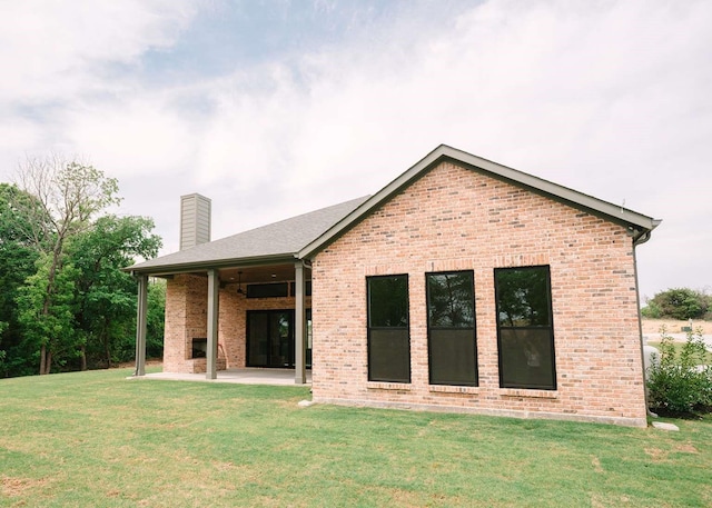 rear view of house with a chimney, a yard, a patio area, and brick siding