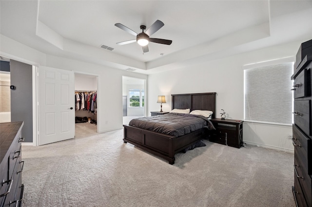 bedroom featuring light colored carpet, a walk in closet, a tray ceiling, and visible vents