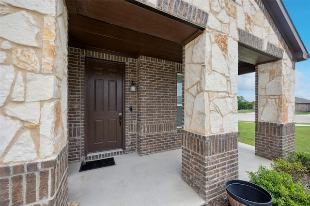 doorway to property featuring stone siding, a porch, and brick siding