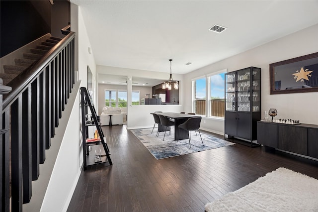 dining space with wood-type flooring, visible vents, an inviting chandelier, baseboards, and stairway