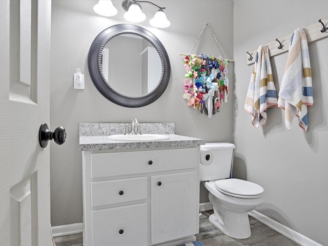 half bathroom featuring baseboards, wood finished floors, toilet, and vanity