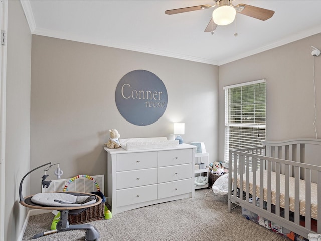 carpeted bedroom with a nursery area, ornamental molding, and ceiling fan
