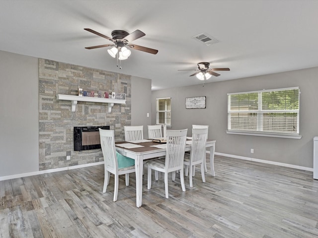 dining space with visible vents, a ceiling fan, wood finished floors, and a stone fireplace