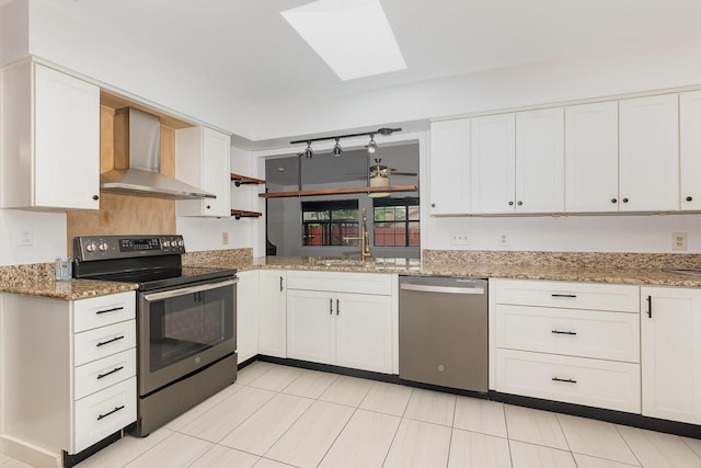 kitchen featuring white cabinetry, appliances with stainless steel finishes, a skylight, and wall chimney range hood