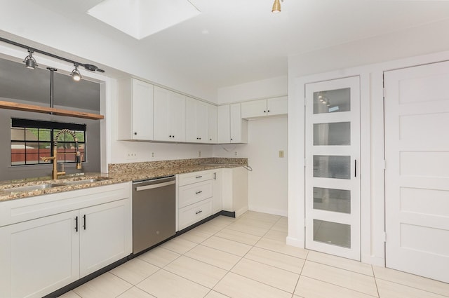kitchen featuring white cabinets, light stone countertops, a sink, stainless steel dishwasher, and a skylight