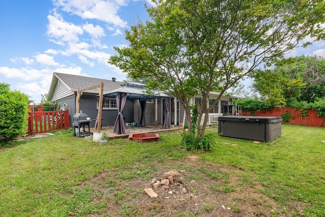 rear view of house with a gazebo, a fenced backyard, a hot tub, and a lawn