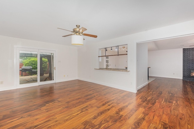 unfurnished living room with a brick fireplace, ceiling fan, baseboards, and wood finished floors