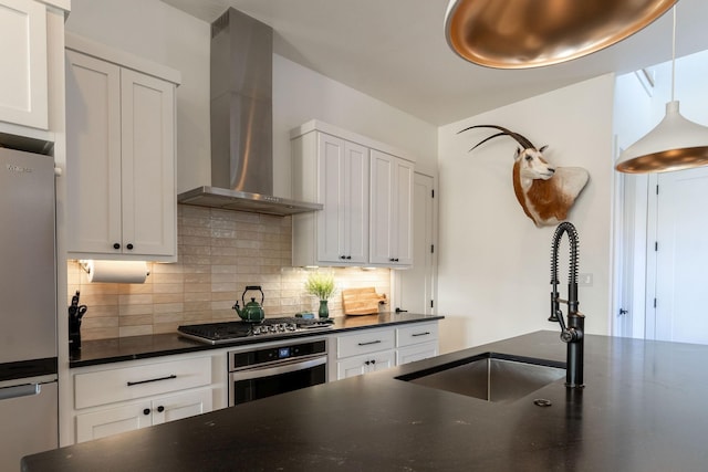 kitchen with appliances with stainless steel finishes, a sink, wall chimney exhaust hood, white cabinetry, and backsplash