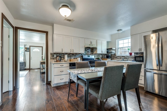 kitchen featuring under cabinet range hood, appliances with stainless steel finishes, decorative backsplash, and visible vents