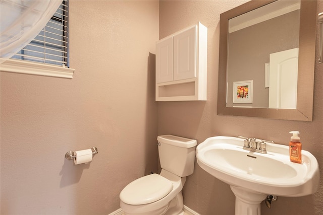 bathroom featuring baseboards, a sink, a textured wall, and toilet