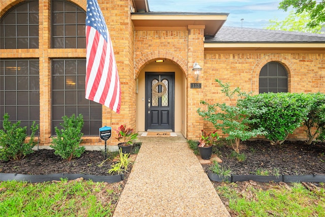 view of exterior entry with a shingled roof and brick siding